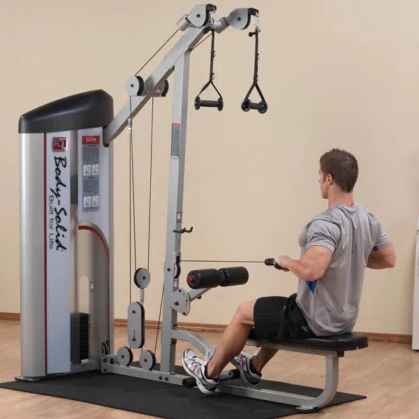 A person performs a cable row on the Body-Solid Pro Clubline Lat Pulldown and Row Machine (S2LAT), featuring weight stacks, adjustable pulleys, and cables in a room with wooden flooring and neutral-colored walls, ideal for strength training.