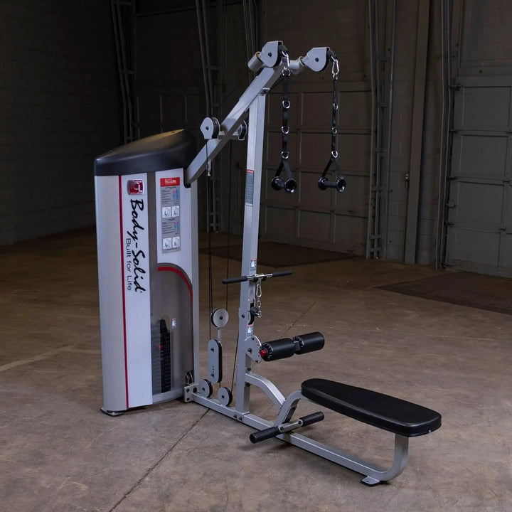 The Body-Solid Pro Clubline Lat Pulldown and Row Machine (S2LAT) with a seated bench, pulleys, and cables for arm exercises stands out in an empty concrete gym. Visible adjustable weight plates enhance any strength training routine.