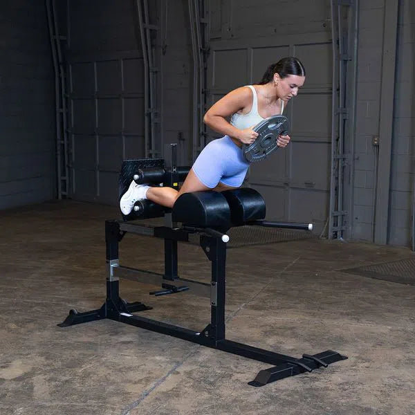 A woman training with a weight plate on Body-Solid Back Hyperextension SGH500