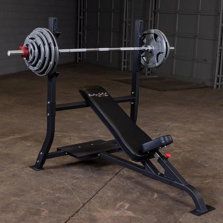 The Body-Solid Pro Clubline Olympic Incline Bench (SOIB250), perfect for upper body workouts, sits on a concrete floor with a black cushioned seat and backrest. A barbell with multiple weight plates complements the garage or gym setting, showcasing premium commercial fitness equipment.