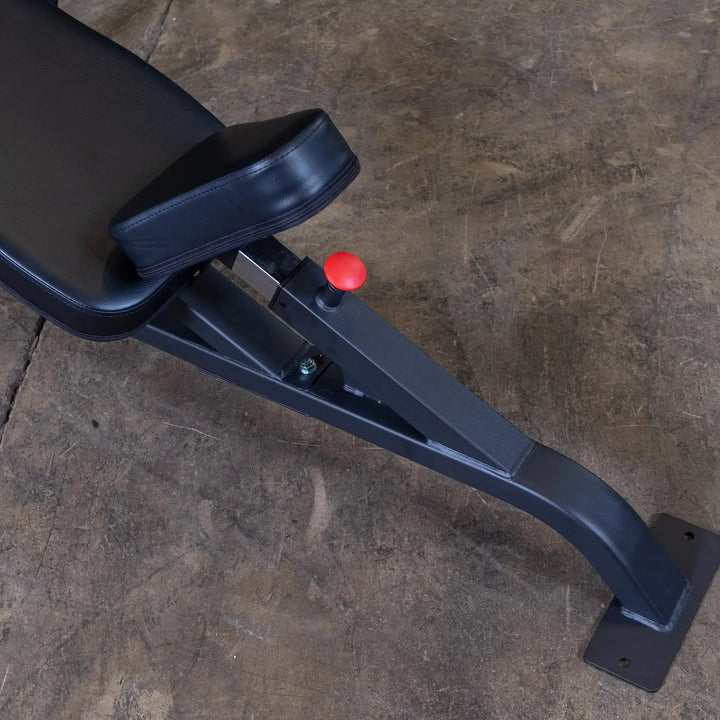 The Body-Solid Pro Clubline Olympic Incline Bench (SOIB250) is a black adjustable gym bench ideal for upper body workouts. It features a red adjustment knob, rests on a textured concrete floor, and boasts a sturdy metal frame for incline exercises.