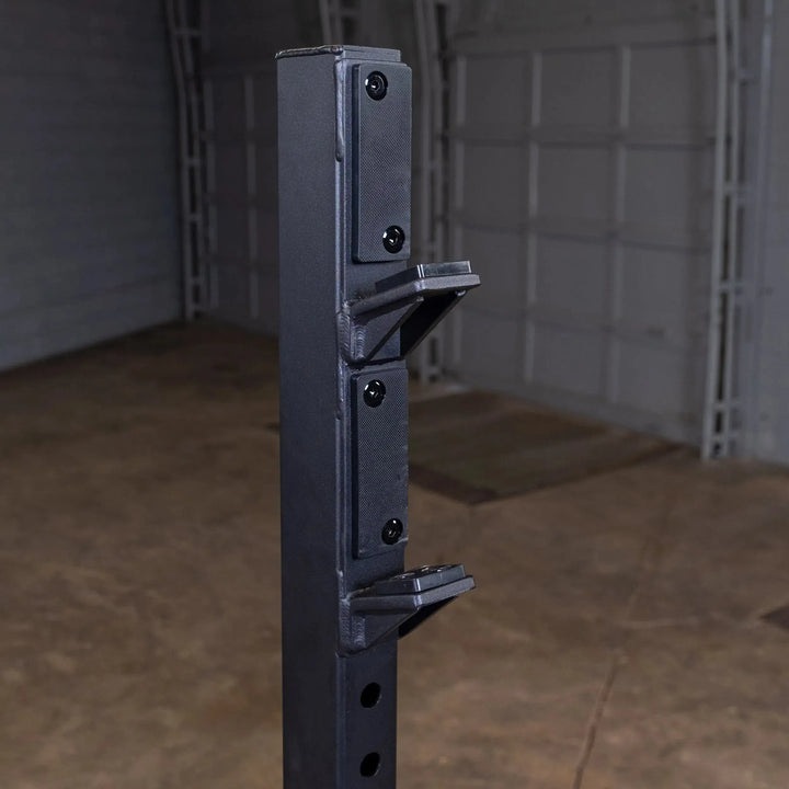 A close-up of a heavy-duty black metal pole with adjustable brackets, part of fitness equipment crafted from steel, is set against a garage backdrop with concrete flooring and a partially closed door—ideal for supporting your Body-Solid Pro Clubline Olympic Shoulder Press Bench (SOSB250).