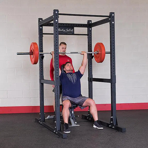 A trainer spotting a man doing shoulder presses on the Body-Solid Commercial Power Rack SPR1000
