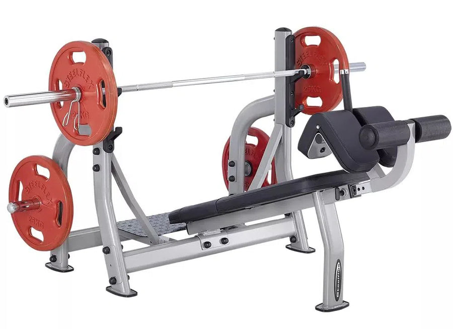 The SteelFlex Olympic Decline Bench (NODB) by Steelflex offers a silver barbell, red weight plates, and black cushioning. Ideal for strength training with incline versatility, it features a footrest and padded areas for comfort and support during rigorous workouts.