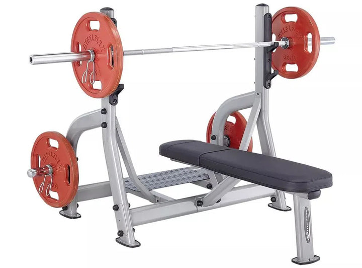 The SteelFlex Olympic Flat Bench (NOFB) by Steelflex features a black padded bench with a sturdy silver frame, commercial-grade quality, and includes a barbell with red weight plates on a sleek rack set against a pristine white background.