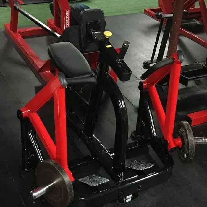 A SteelFlex Chest Supported Row Machine (PLSR) by Steelflex, in striking red and black, sits in the gym with an ergonomic design featuring a padded seat and footrests. Weights rest on black mats beside it, while another commercial-grade piece of equipment peeks into view.