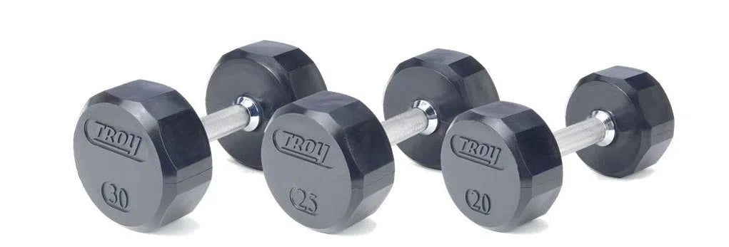Four Troy rubber dumbbells with silver handles are displayed in a staggered row, emphasizing their commercial quality. Weights of 30, 25, and two at 20 lbs rest on a plain white background, highlighting built-in safety features for workout peace of mind. Brand: TROY Barbell.