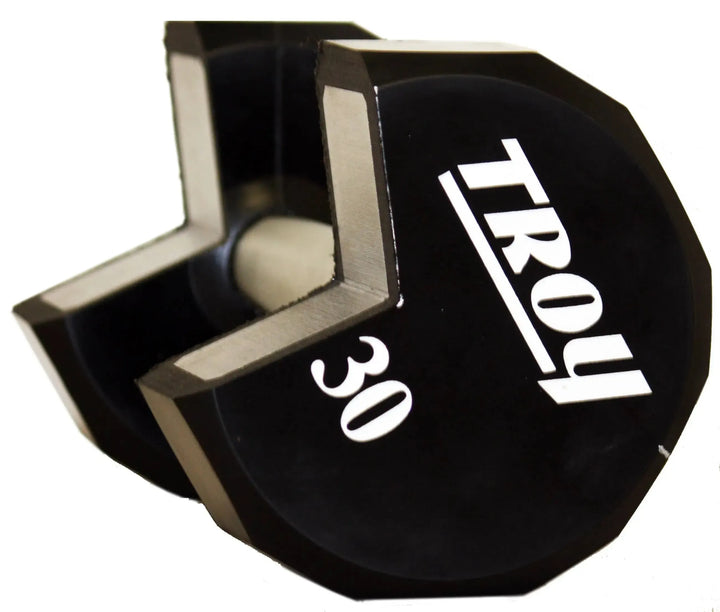 A black 30-pound dumbbell from the Troy 5-50 lb Urethane Commercial Dumbbell Set with hexagonal ends lies on its side, featuring TROY Barbell in white. Ideal for fitness enthusiasts seeking durable, high-quality equipment.
