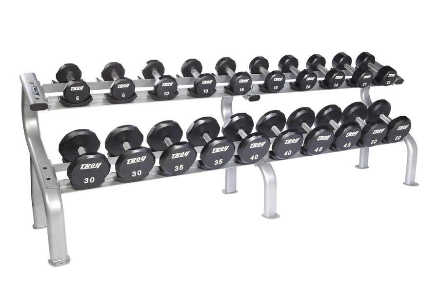 The TROY Barbell two-tier rack holds the Troy 5-50 lb Urethane Commercial Dumbbell Set, featuring black dumbbells with white-labeled numbers and a sleek silver metallic frame.
