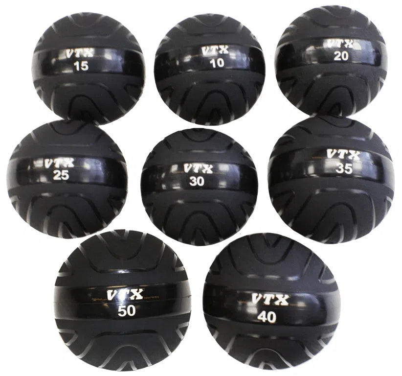 The VTX Slam Ball Set includes seven black medicine balls, ideal for commercial gyms, in two rows. Each ball shows weights from 15 to 40 pounds and features the VTX logo. Designed for strength-training, they have textured grips for optimal handling.