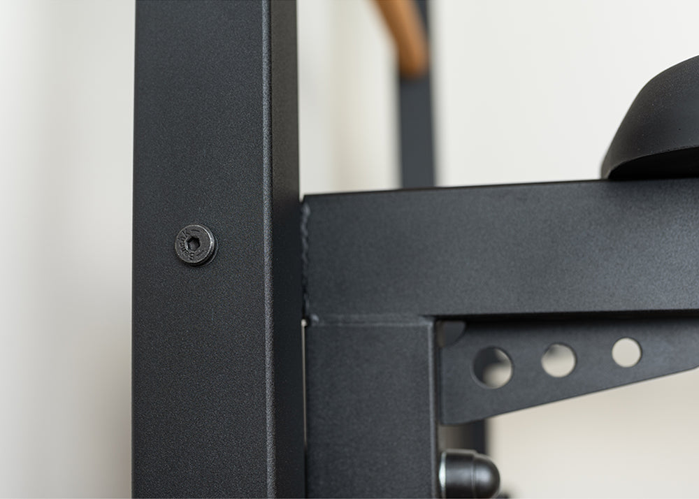 Close-up of a black metal frame from the BenchK Pro Gym Wall Bars w/ Bench, Dip & Flex Pull-Up Bar (733), highlighting a corner joint with a bolt and multiple adjustment holes for multifunctionality like a pull-up bar; features a sleek, smooth finish.