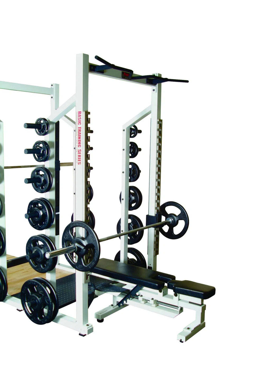 The setup includes a York Barbell STS Double Half Rack, ideal for strength training. This white squat rack has weight plates on side pegs, a barbell on safety catches, an adjustable bench underneath, and a pull-up bar at the top.