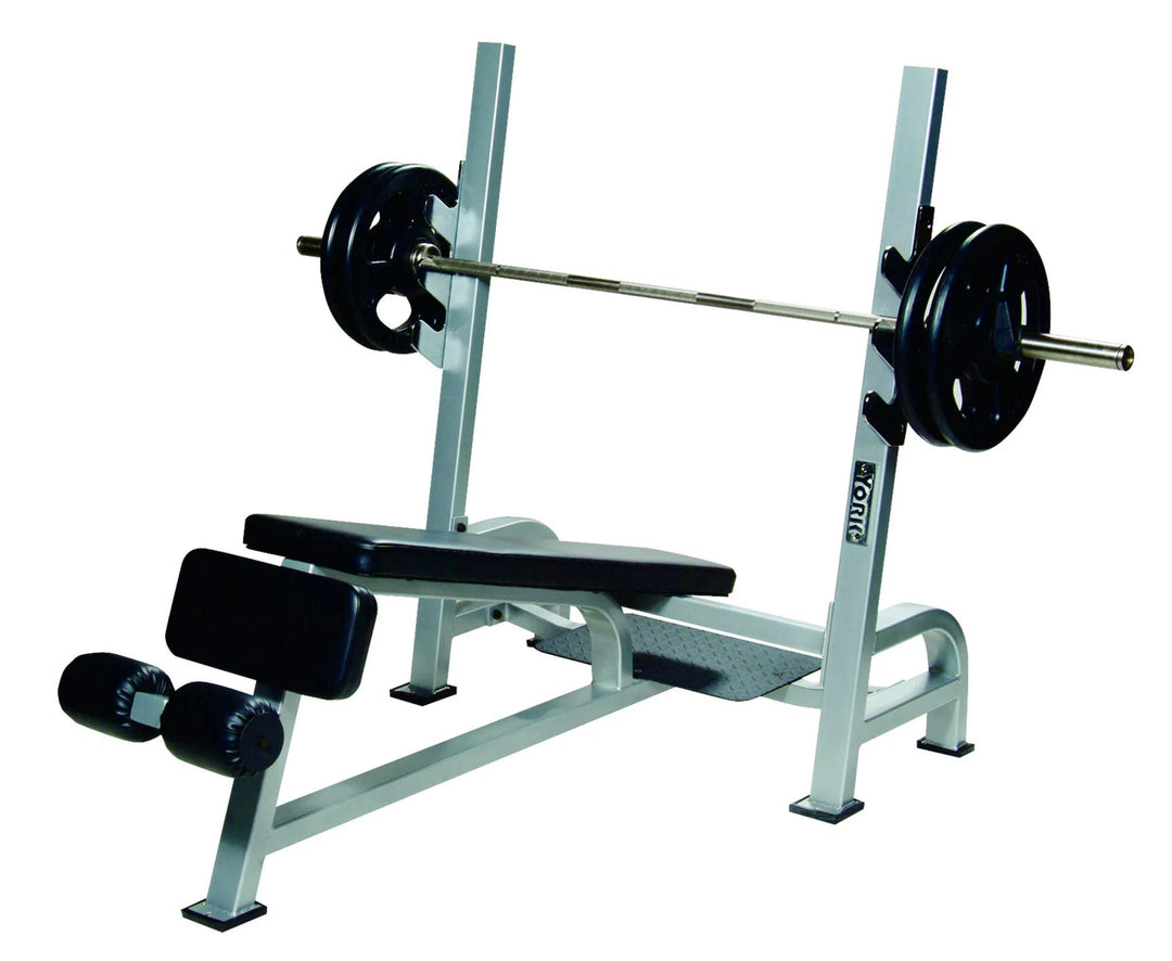 The York Barbell STS Olympic Decline Bench Press features contour foam padding for ultimate comfort, a black and gray metallic frame with polished chrome bar holders, padded bench, footrests, and vertical supports.