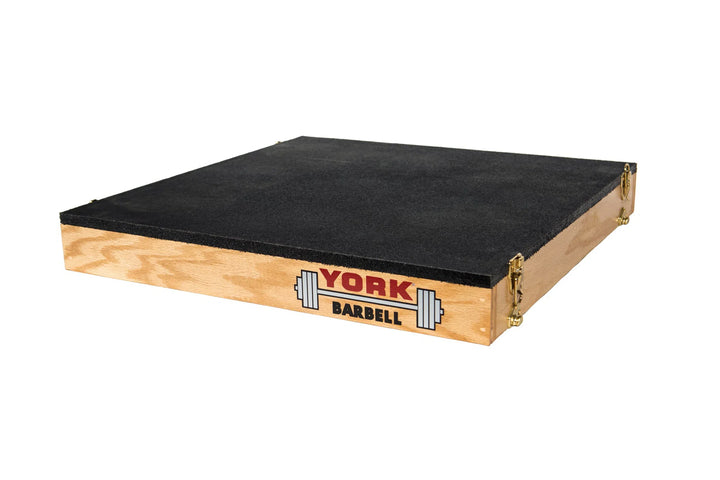 The York Stackable Plyo / Step-Up Box by York Barbell is a wooden platform with a black top and the brands barbell logo on the side. Ideal for high-intensity workouts, it features metal-reinforced edges, highlighted on a white background to showcase its sturdy construction.