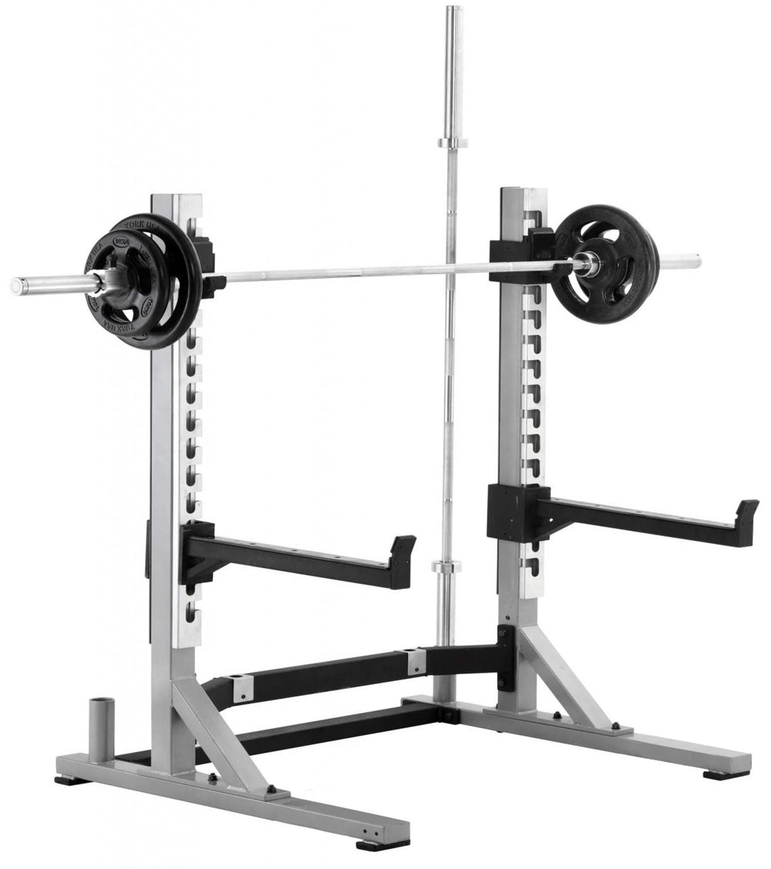 The York Barbell STS Collegiate Squat Rack is compact, with adjustable supports and safety catches. A barbell with weight plates sits at shoulder height, perfect for strength training enthusiasts ready for their next lift.