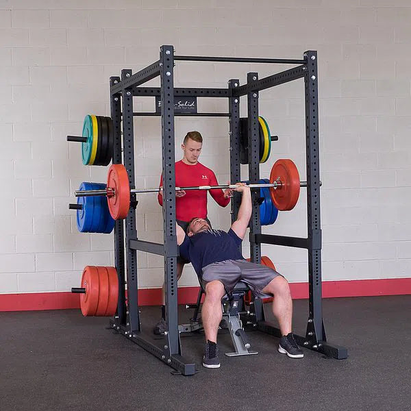 man being spotted doing bench presses in power rack