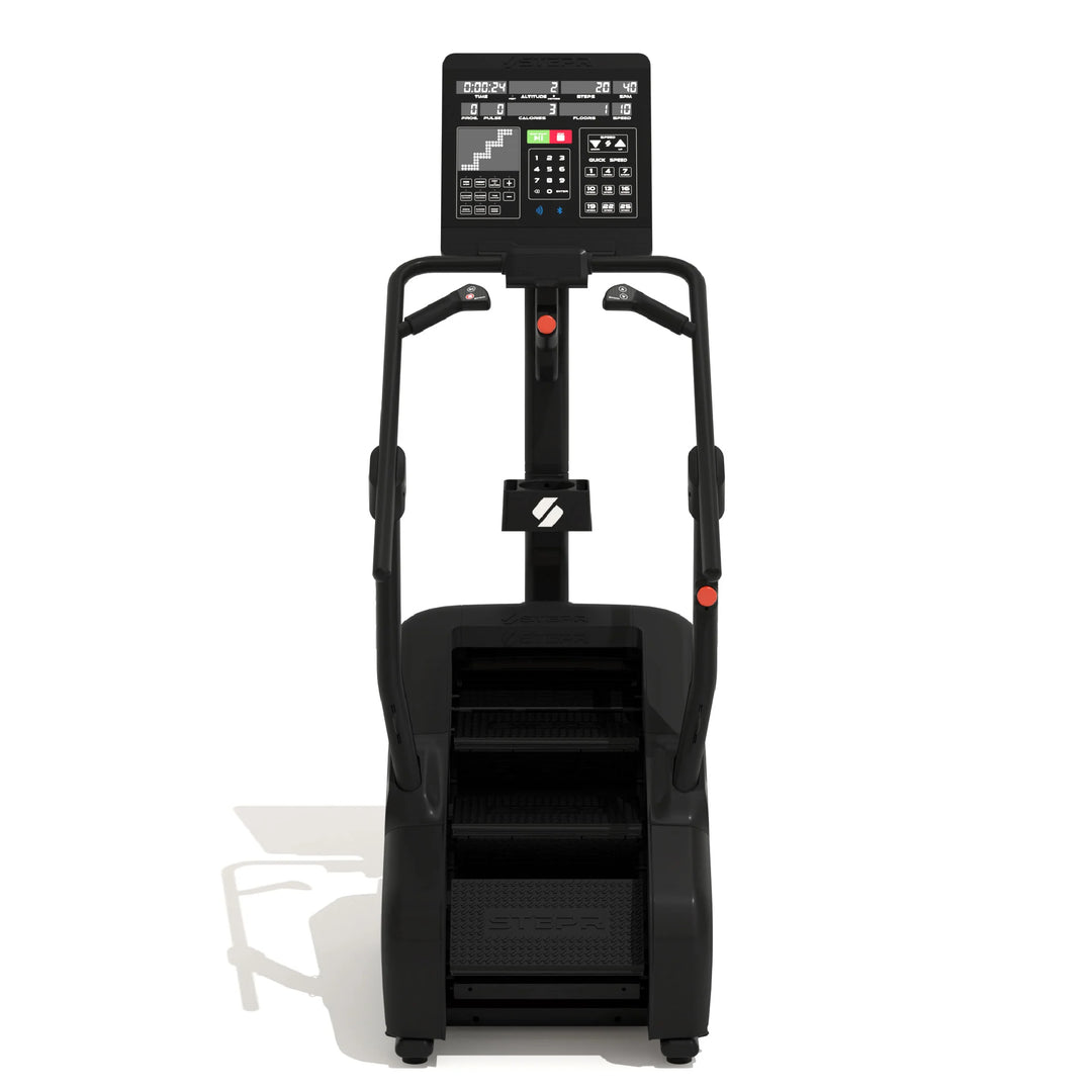 A black, upright exercise machine with stair steps and handlebars. It has a digital display screen at the top showing various settings. The floor casts a shadow from the machine.