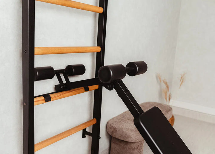 A fitness area features the BenchK Pro Gym Wall Bars with a bench, dip & flex pull-up bar offered by BenchK, integrated with multifunctional equipment like black padded handles. The rooms light-colored walls and gray furniture complement this sleek setup.