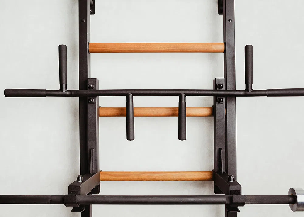 Introducing the BenchK Pro Gym Wall Bars w/ Bench, Dip & Flex Pull-Up Bar (733) by BenchK, boasting sleek wooden bars and sturdy black metal handles. Perfect for strength training, its elegant design adds sophistication to any fitness space with a light gray backdrop.