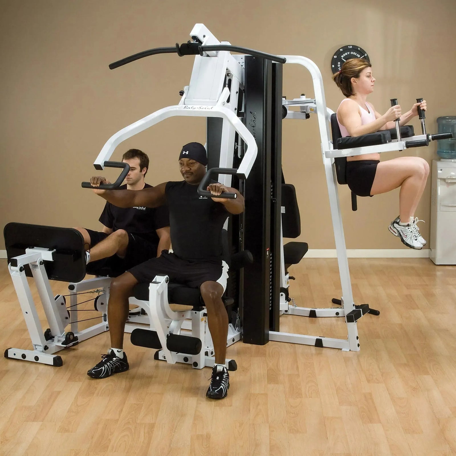 A group of 3 people training together on the Body-Solid Universal Weight Machine with Leg Press EXM3000LPS