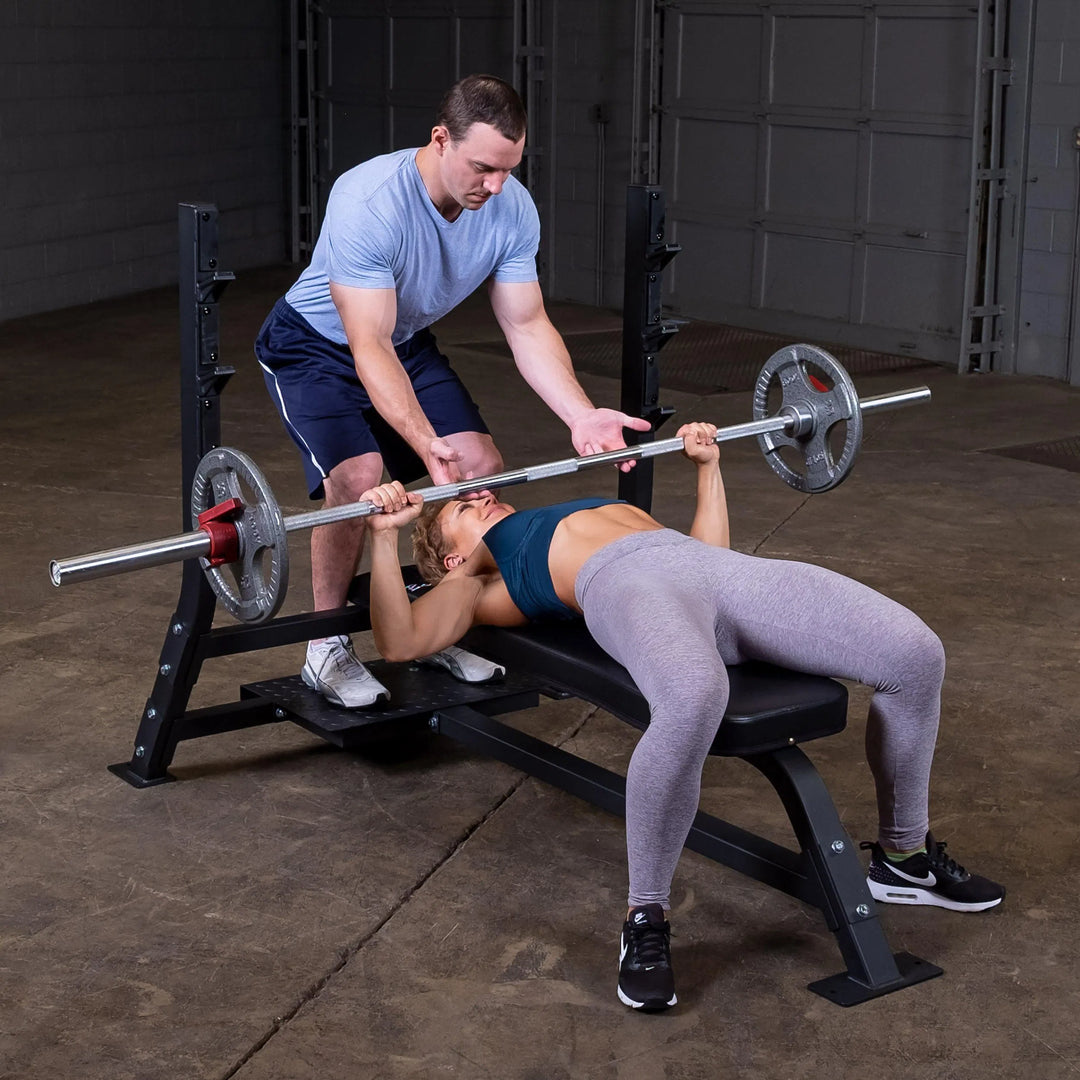 A man spotting a woman doing bench presses on the Body-Solid Commercial Olympic Flat Bench SOFB250