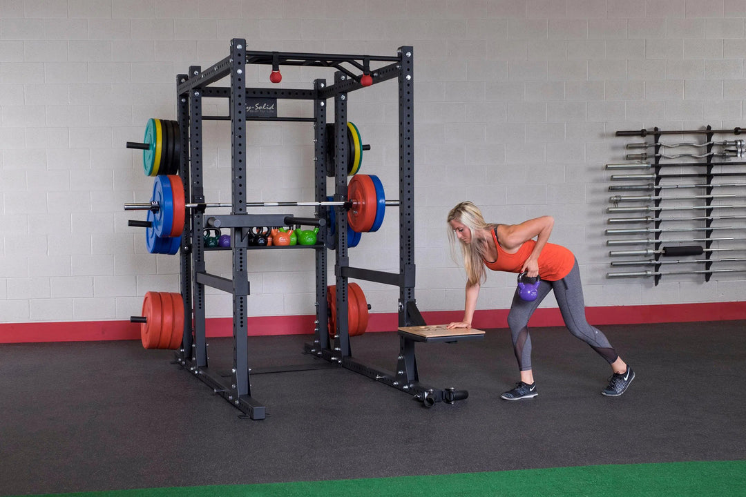 A woman showcasing attachments for the Body-Solid Commercial Power Rack Extended SPR1000Back