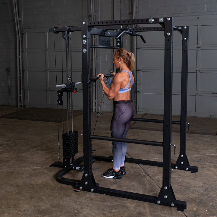 Woman doing a standing high pulley row on a Body-Solid GPR400 power rack fitted with the GLA400 lat attachment and a selectorized weight stack