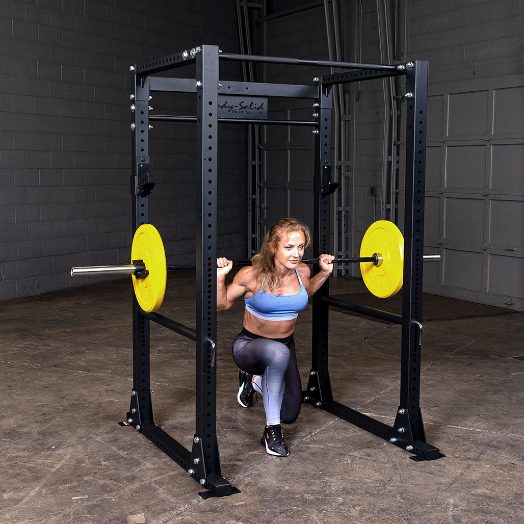 Woman at the bottom of a back squat inside a Body-Solid GPR400 power rack, barbell loaded with yellow bumper plates