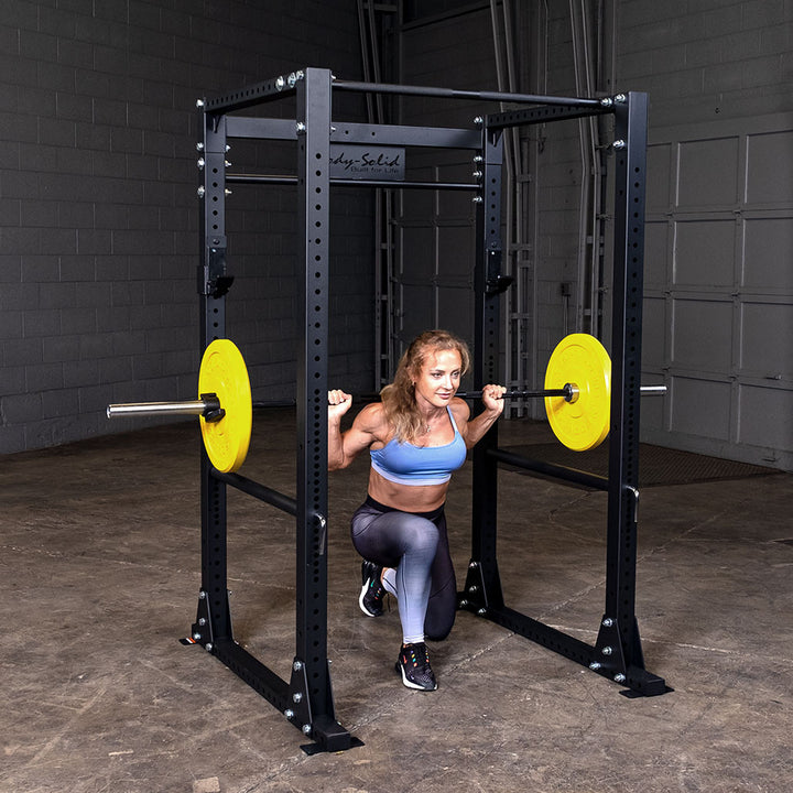 Woman at the bottom of a back squat inside a Body-Solid GPR400 power rack, barbell loaded with yellow bumper plates
