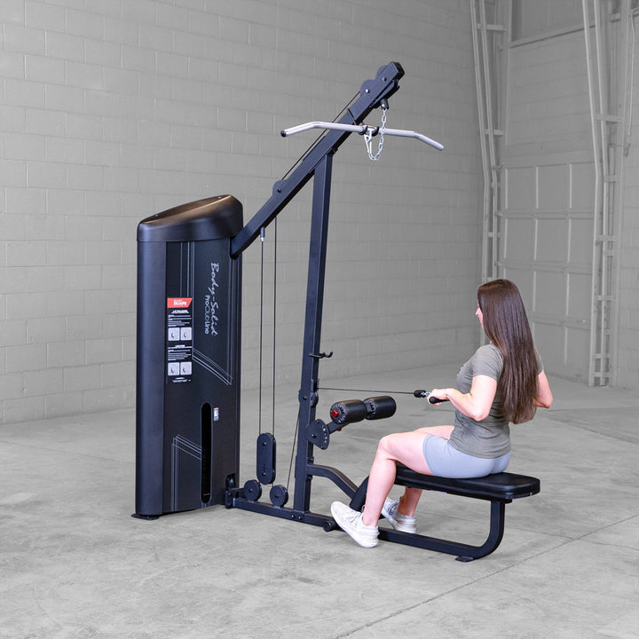 Body-Solid S2LATX commercial lat pulldown station in use, with a lifter seated under the thigh pad pulling the lat bar down.