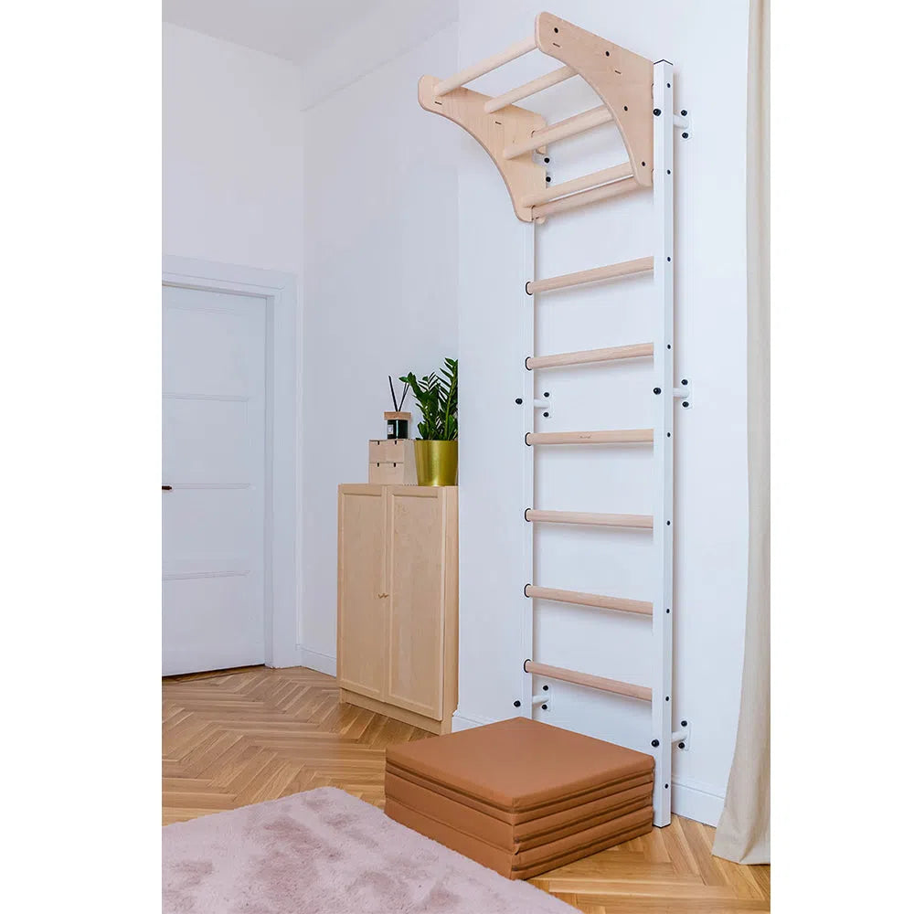 The BenchK Home Stall Bars (711) with a wooden pull-up bar, mounted beside a cabinet with potted plants, set the tone in this chic home gym. Stacked beige mats, light walls, and herringbone flooring create a serene space perfect for any fitness routine.