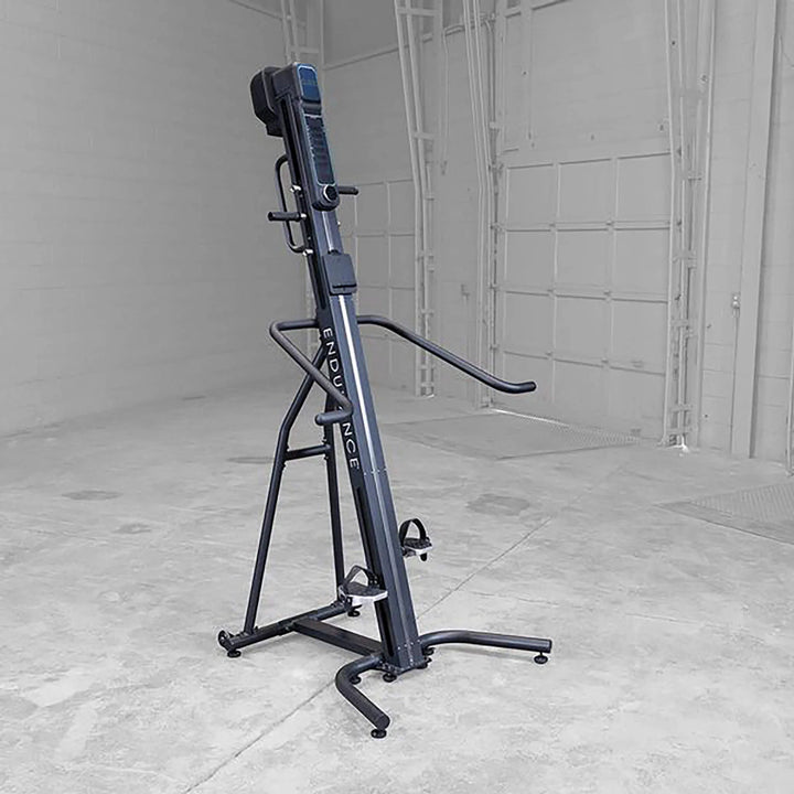 The Body-Solid Endurance Mountain Climber Machine (CL300) is in a gray-walled, empty room on a concrete floor. This equipment features a tall frame with handles and foot pedals, and it provides adjustable resistance for tailoring full-body workouts to any fitness level.