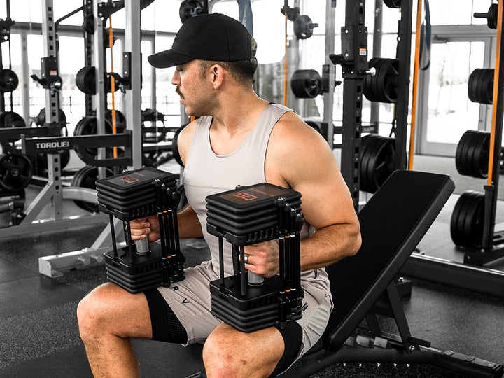 Lifter holding a pair of PowerBlock Commercial Pro 100 dumbbells set to 50 lb per hand before a bench press