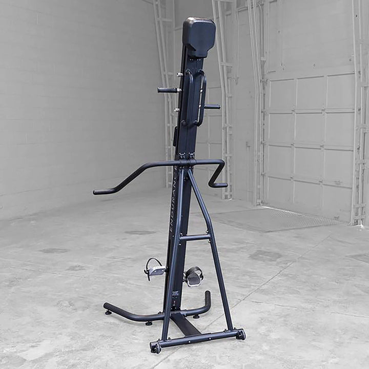 The Body-Solid Endurance Mountain Climber Machine (CL300) is set against an industrial backdrop with a white garage door and concrete floor. It features adjustable resistance, handlebars, foot pedals, and a cushioned seat back for a full-body workout.