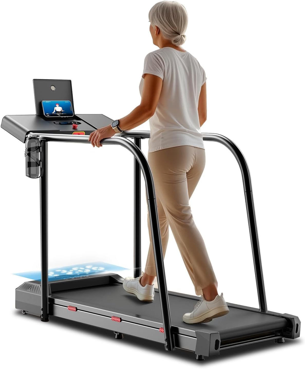 An older woman with gray hair walks on a treadmill, facing a screen on the console. She wears a white t-shirt, beige pants, and white sneakers. The treadmill has handrails and a water bottle holder.