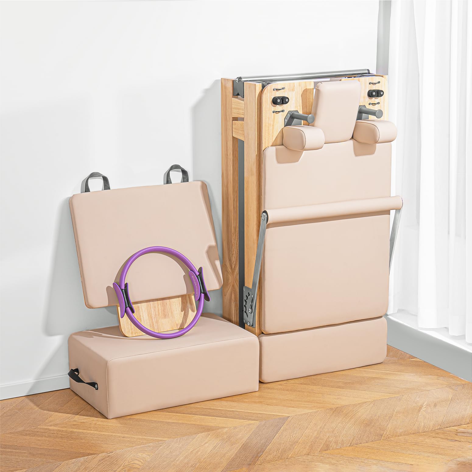 Two pieces of light beige exercise equipment are placed on a wooden floor by a white wall and window. One piece is folded upright, while the other is open with a purple fitness ring resting on it.