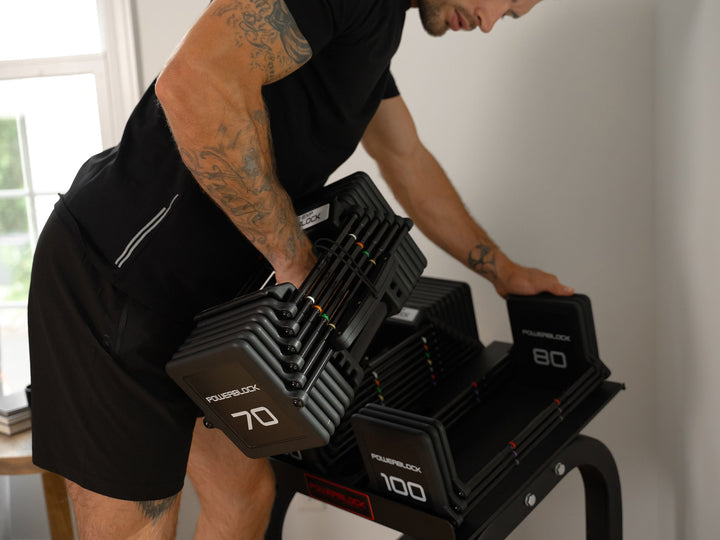 Athlete lifting 70 lb PowerBlock Pro 100 EXP dumbbells off a PowerBlock stand in a home gym