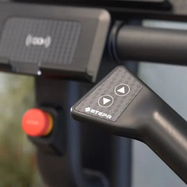 Close-up of the STEPR PRO Classic Stair Climber handle featuring up/down arrow buttons perfect for High-Intensity Training. In the background, a red emergency stop button and digital screen mount are visible. The STEPR brand name enhances the classic design excellence of this equipment.