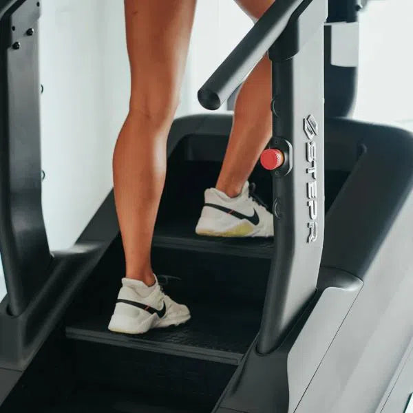 Close-up of someone in white sneakers and black shorts using the STEPR PRO+ Commercial Stair Climber by STEPR, highlighting their legs and the steps of the fitness machine during an intense workout.