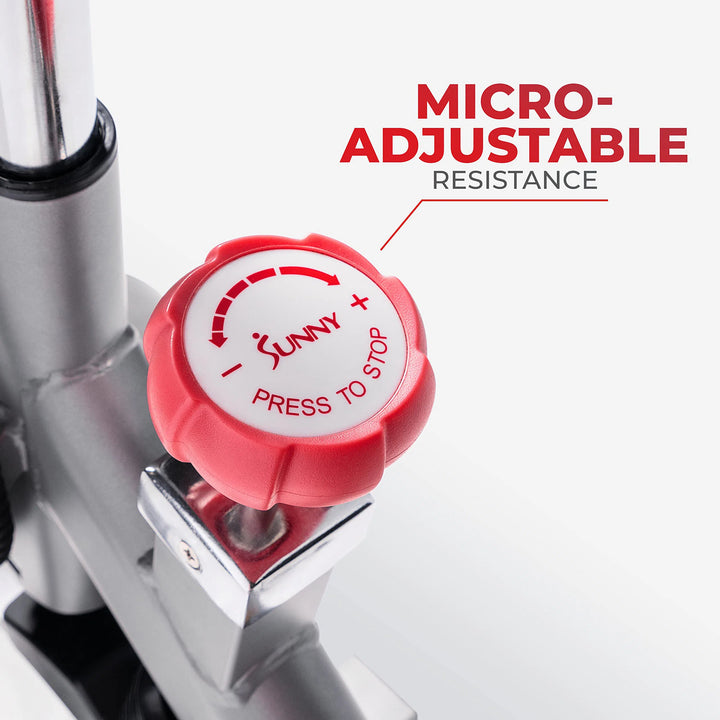 A close-up highlights the red resistance knob on the Sunny Health & Fitness Synergy Series bike, labeled Press to Stop with Micro-Adjustable Resistance in vibrant red text overhead. An arrow points to it, emphasizing precise workout control.